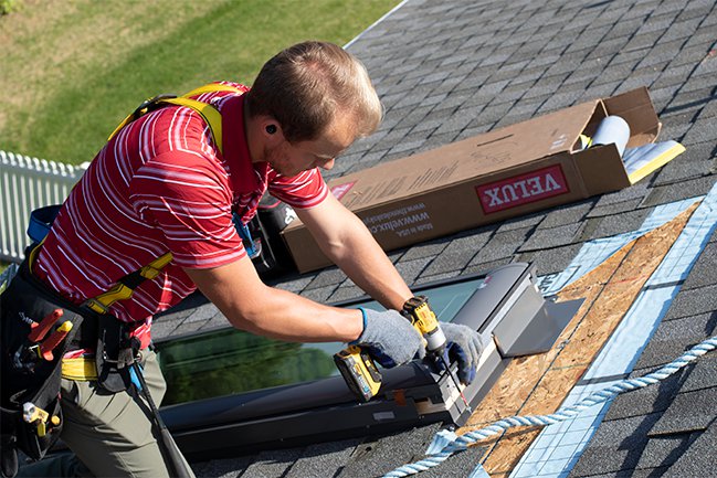 A roofer installing a skylight unit on a roof.